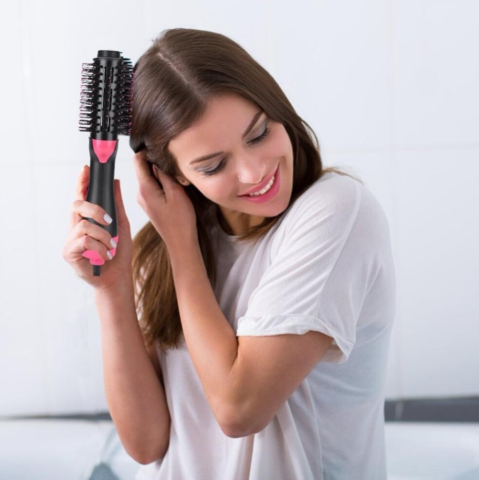 Woman styling long brown hair with a black and pink one-step electric hot air brush hair dryer for fast drying, volumizing, smoothing, straightening, frizz reduction and salon-style blowouts at home