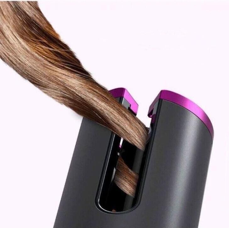 Wireless automatic electric hair curler styling a smooth brown hair strand with a rotating ceramic curling barrel, cordless portable curling iron for creating defined curls, loose waves and salon-quality hairstyles at home or while traveling.
