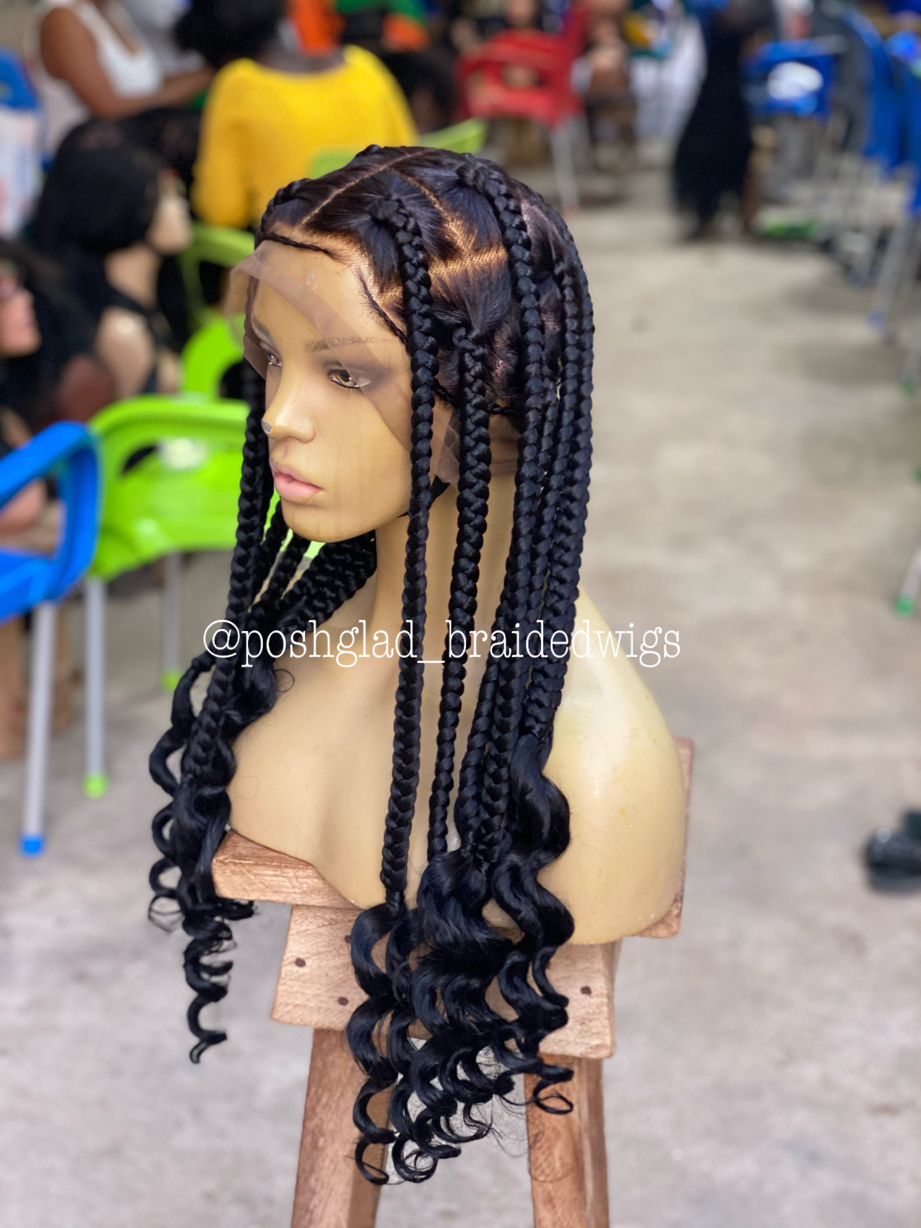 Mannequin head with braided wig on a wooden stool in a store setting. jumbo knotless braid wig, knotless braid wig, jumbo braid wig, braided wig, full lace braided wig, swiss lace wig, swiss full lace wig, glueless braided wig, glueless wig, human hair braided wig, 100% human hair wig, knotless braids, jumbo knotless braids, scalp looking wig, natural scalp wig, lace braid wig, handmade braided wig, handcrafted wig, black braided wig, color 1B wig, 1B braided wig, long braided wig, bra strap length wig