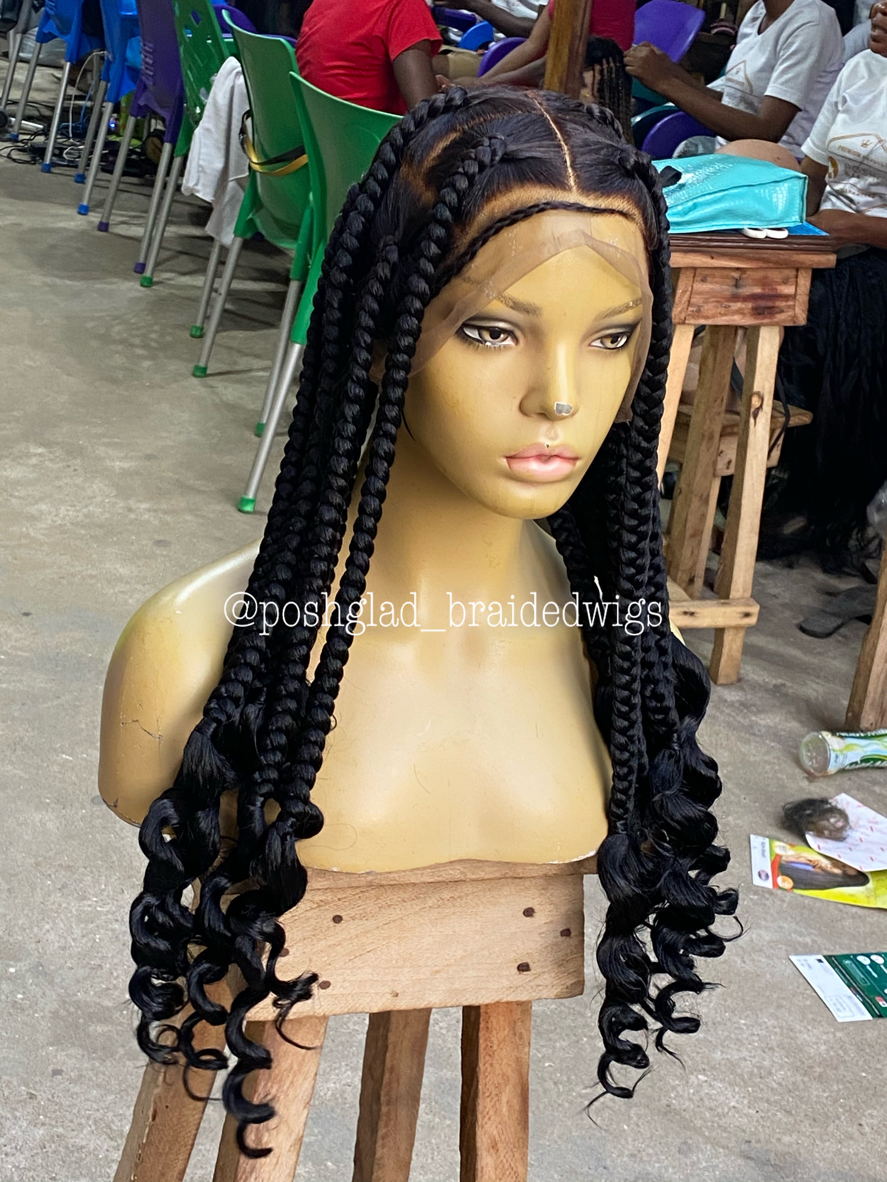 Mannequin head with a black braided wig on a wooden stand in an indoor setting. jumbo knotless braid wig, knotless braid wig, jumbo braid wig, braided wig, full lace braided wig, swiss lace wig, swiss full lace wig, glueless braided wig, glueless wig, human hair braided wig, 100% human hair wig, knotless braids, jumbo knotless braids, scalp looking wig, natural scalp wig, lace braid wig, handmade braided wig, handcrafted wig, black braided wig, color 1B wig, 1B braided wig, long braided wig