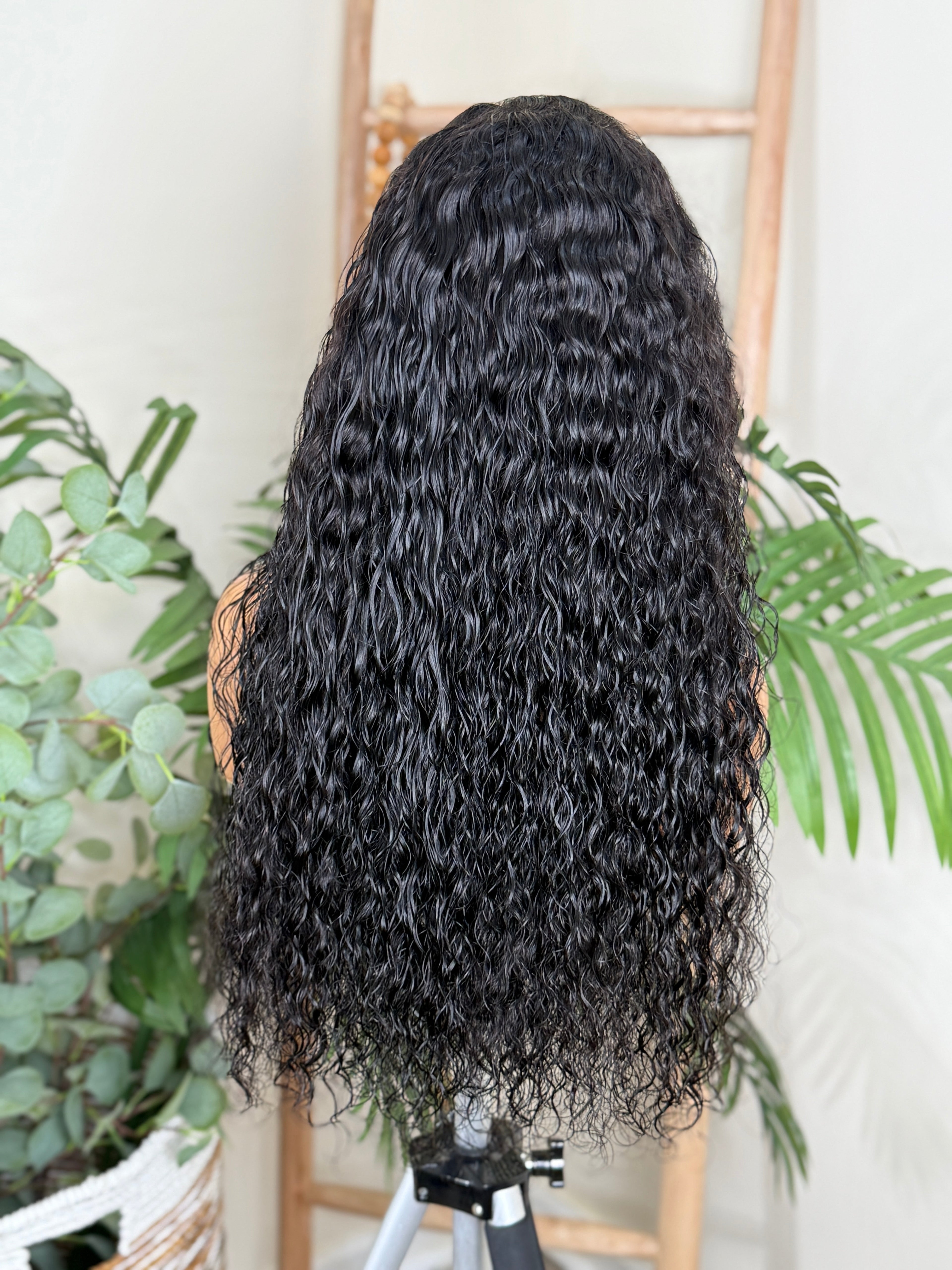 Curly wig on a mannequin head with plants in the background Exotic Curl Virgin Hair - 100% Virgin Human Hair – Bold, voluminous, and full of life HD Glueless Lace WIg