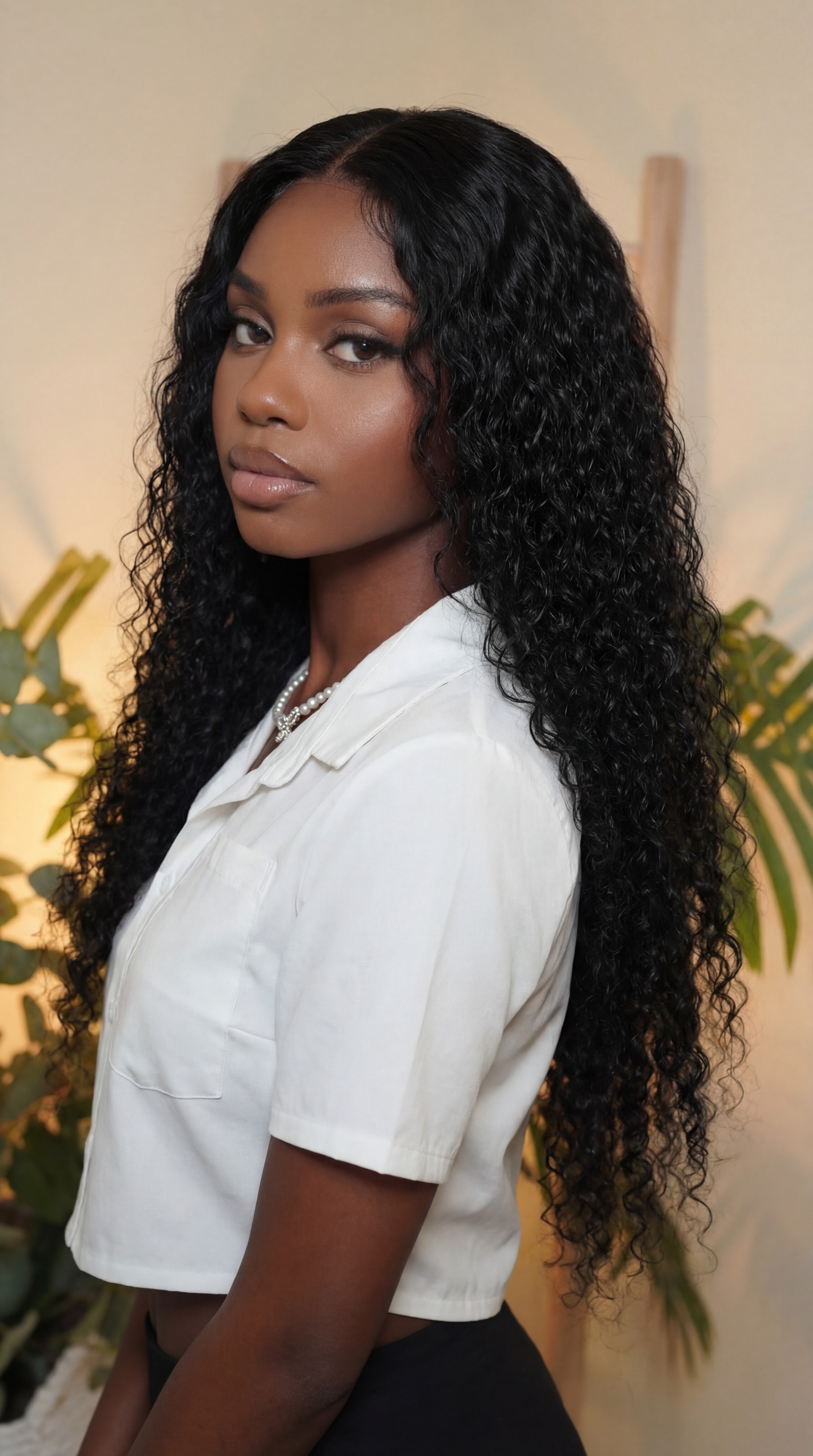 Woman with long, curly black hair wearing a white shirt in a natural setting. Italian Curl Virgin Hair Wig - Made with 100% Virgin Human Hair