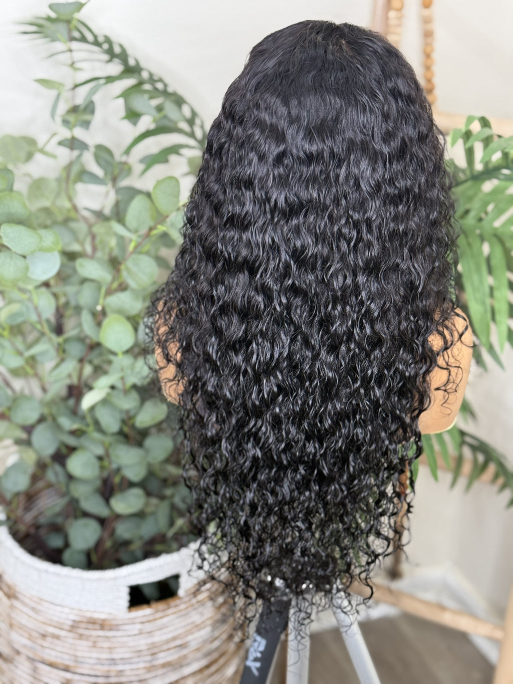 Black curly wig on a mannequin head with plants in the background