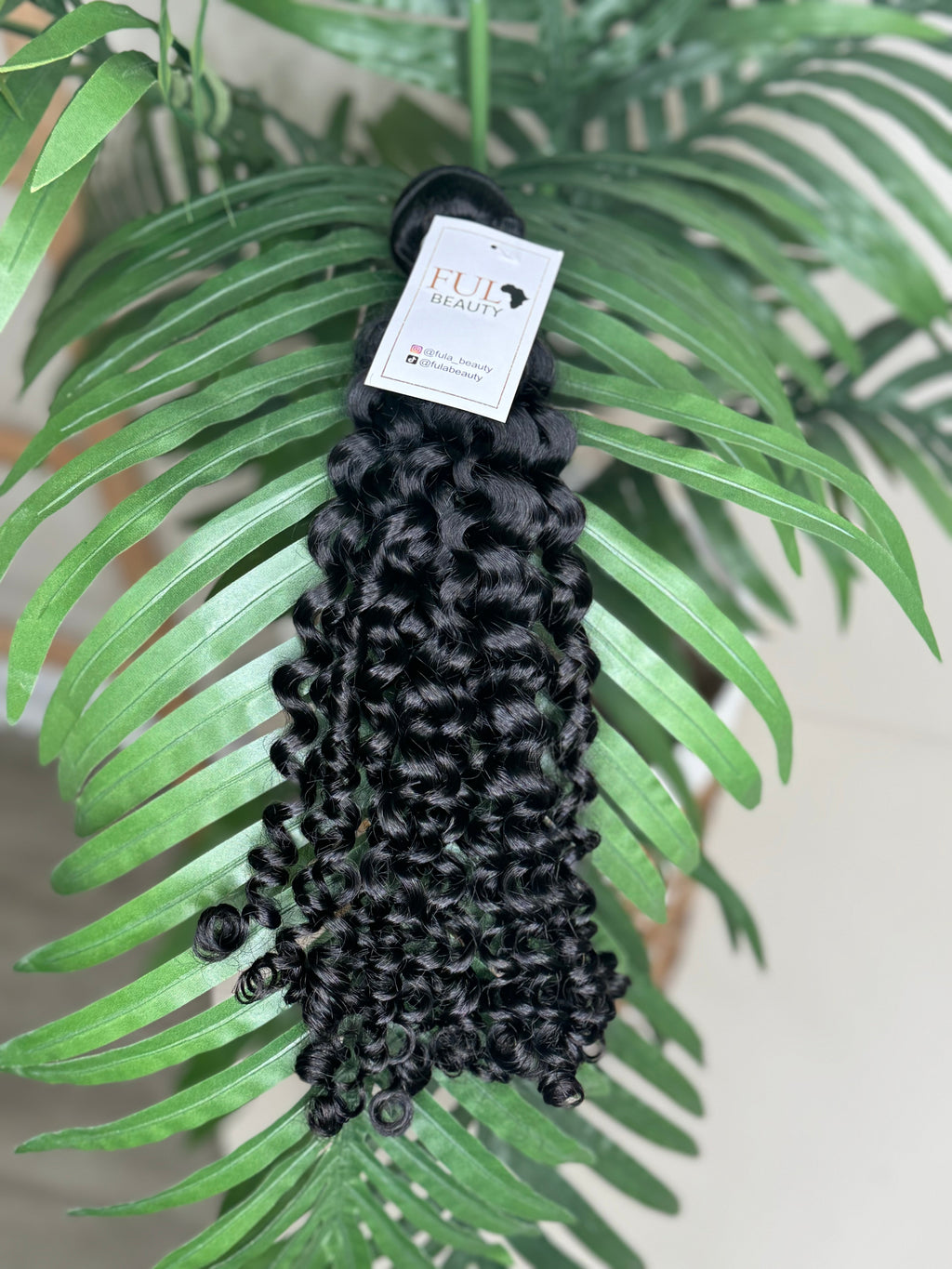 Black hair extensions on a green leafy background with a visible brand label.