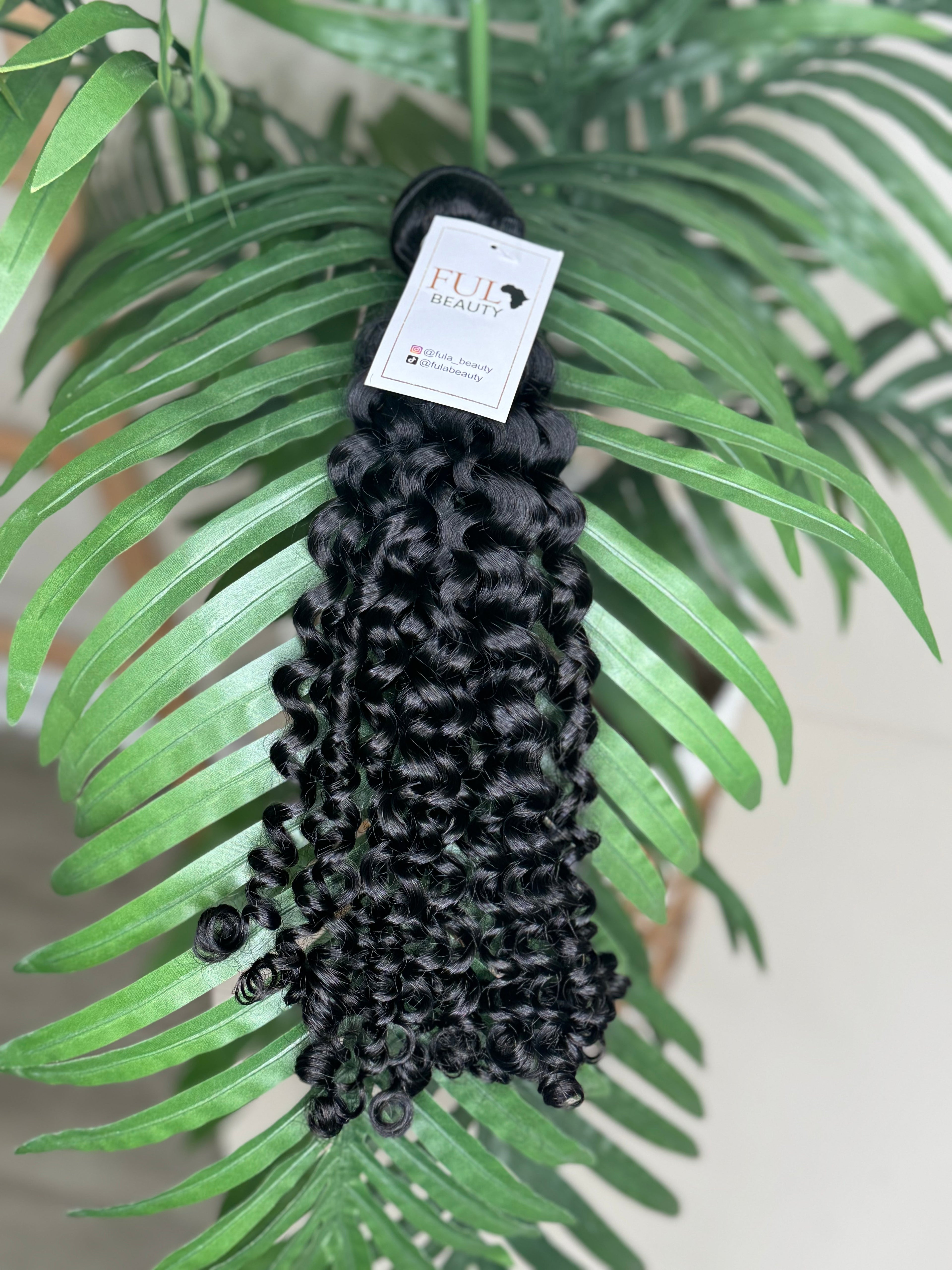 Black hair extensions on a green leafy background with a visible brand label.