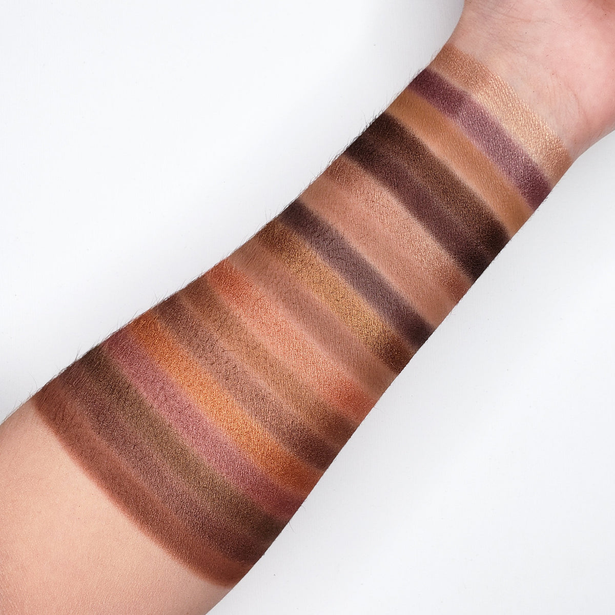 Swatches of brown and beige eyeshadow on a person's arm against a white background