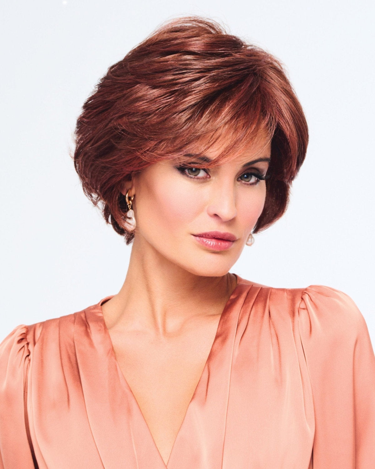 Woman with styled hair wearing a peach top against a light background