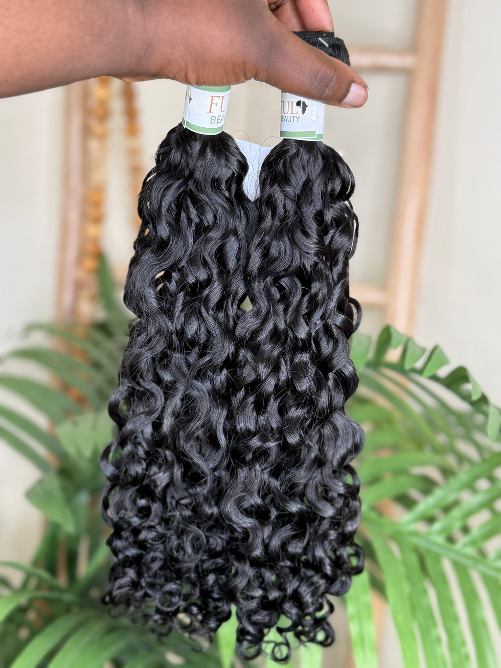 Bundles of curly hair extensions held by a person with a blurred background Water Curly Wefted Bundle - 100% Human Hair, Double Drawn 18" to 26" inch Bundles