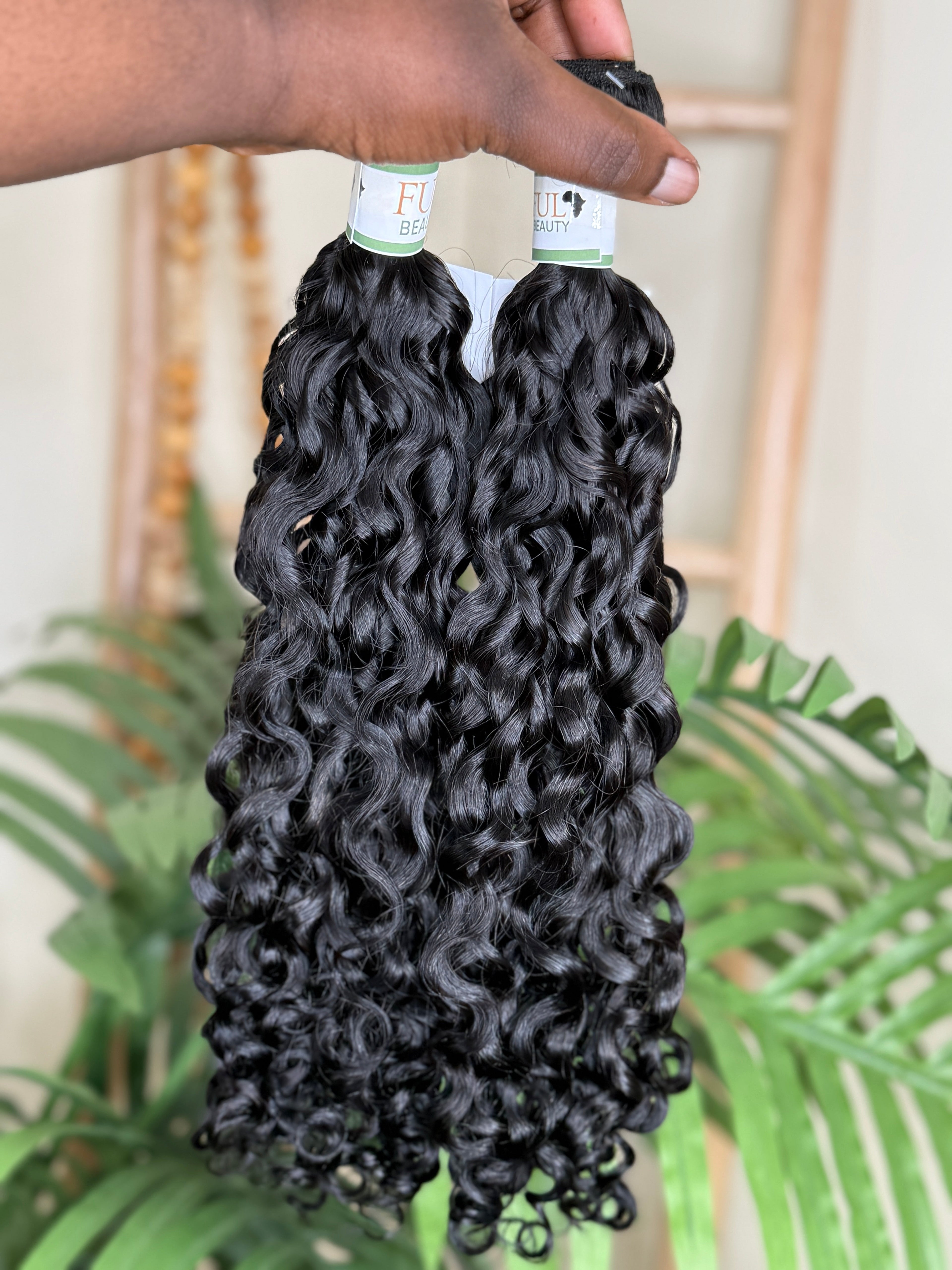 Bundles of curly hair extensions held by a person with a blurred background Water Curly Wefted Bundle - 100% Human Hair, Double Drawn 18" to 26" inch Bundles