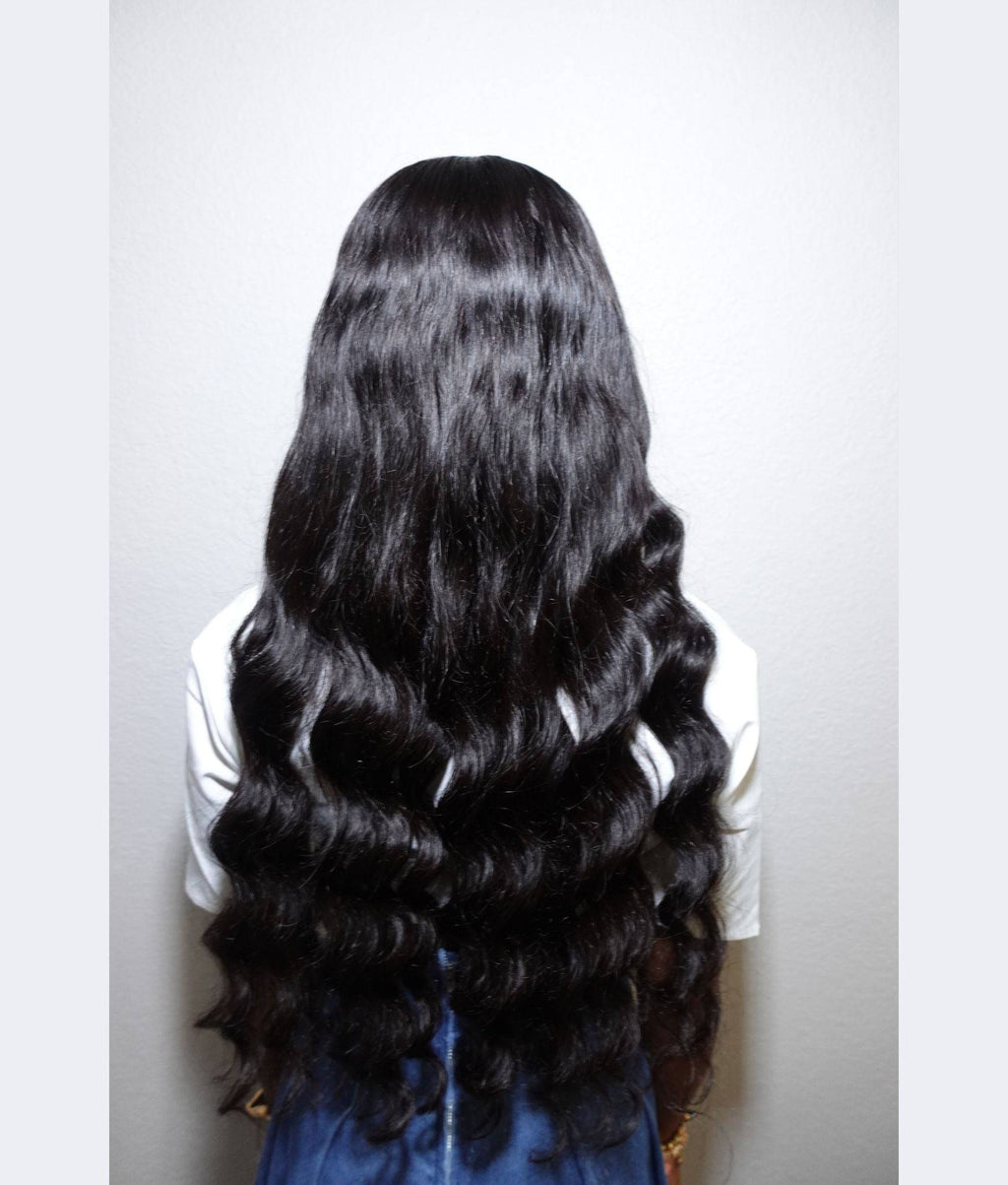 Person with long, wavy black hair on a plain background Body Wave 100% Virgin Human Hair – No tangles, no shedding, all softness. 16”–30”
