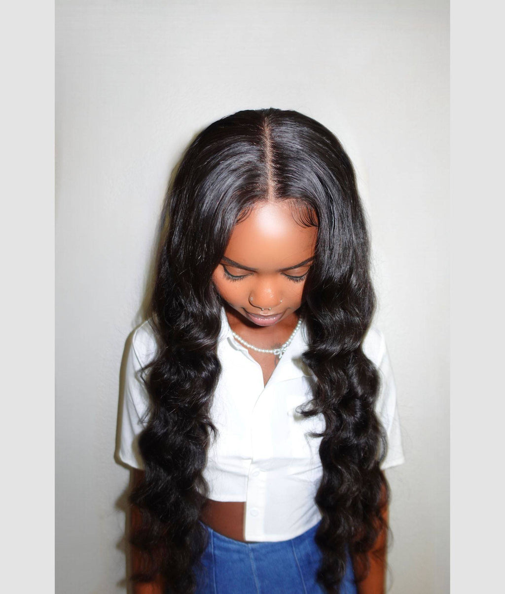 Person with long, wavy hair wearing a white shirt and blue pants against a plain background Body Wave 100% Virgin Human Hair – No tangles, no shedding, all softness. 16”–30”