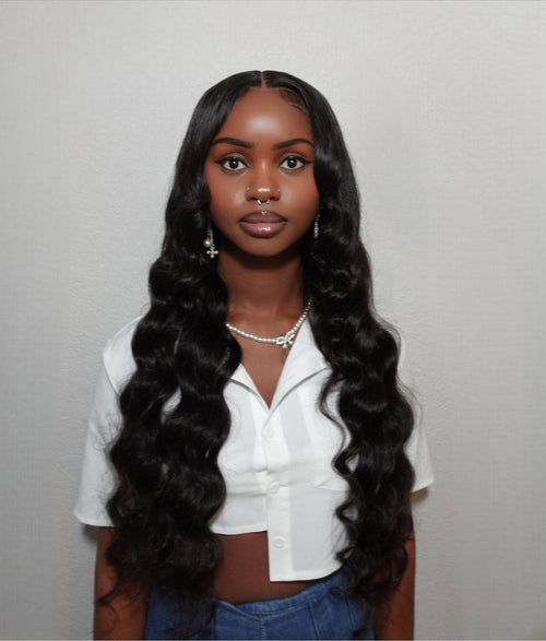 Person with long, wavy hair wearing a white shirt and blue jeans against a plain background Body Wave 100% Virgin Human Hair – No tangles, no shedding, all softness. 16”–30”