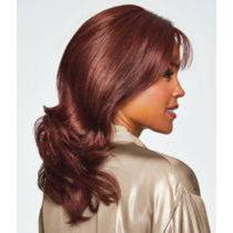 A woman shown in side profile wearing a shoulder-length auburn wig with soft waves and a side-swept bang, against a light gray background.