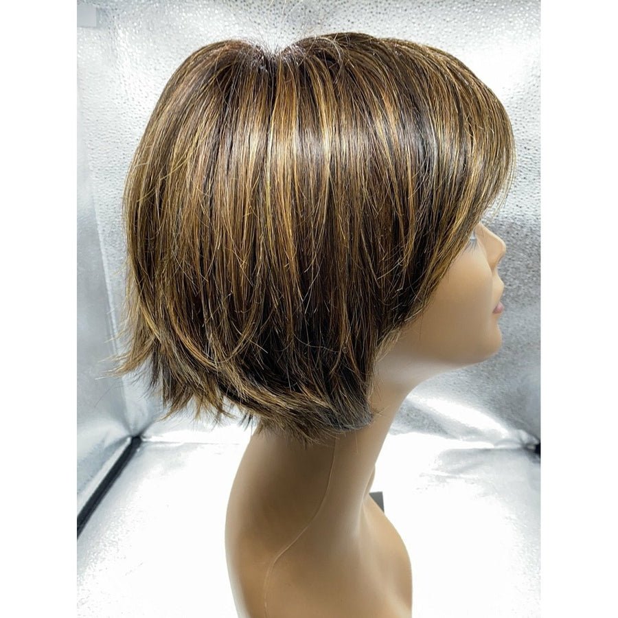 A short layered wig displayed on a mannequin head, photographed against a silver studio backdrop. The wig has a medium brown base with warm caramel and blonde highlights throughout.