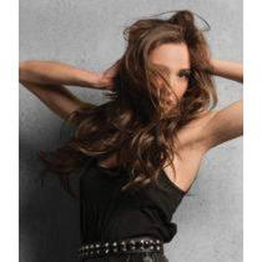 Woman with long brown hair posing against a gray background