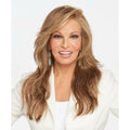 A smiling woman with long, wavy blonde-brown hair wearing a white top, shown from the chest up against a light gray studio background. Miles of Style - Wig by Raquel Welch