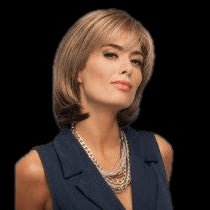 A woman with short blonde hair wearing a navy sleeveless blazer and a chunky silver necklace, shown against a solid black background.
