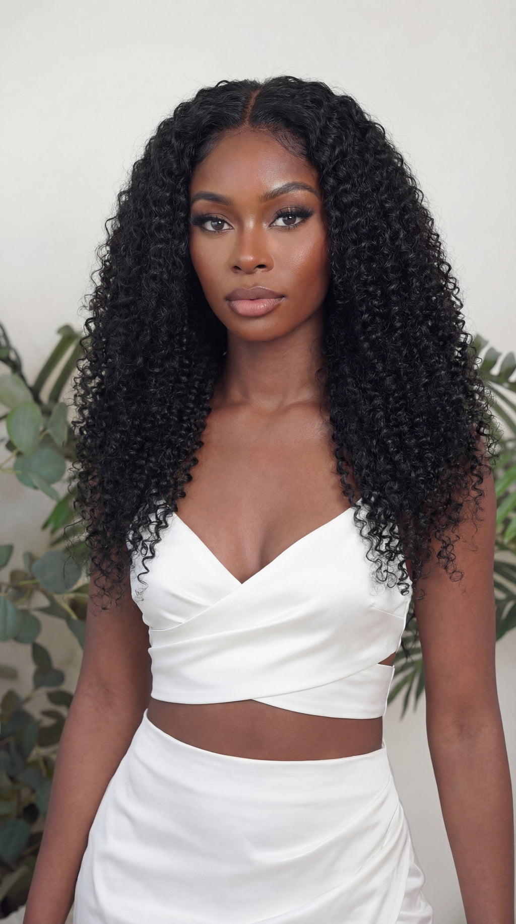 Woman with long, curly hair wearing a white outfit against a neutral background